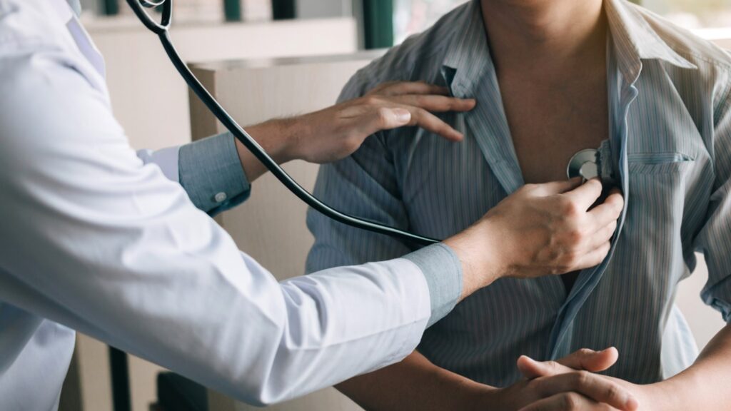 A doctor holds a stethoscope up to the chest of a patient.