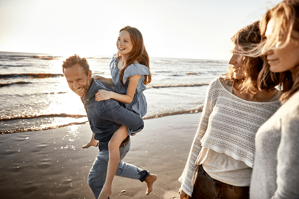 A family enjoying a sunny day at the beach, playing together with their child in the sand and surf.