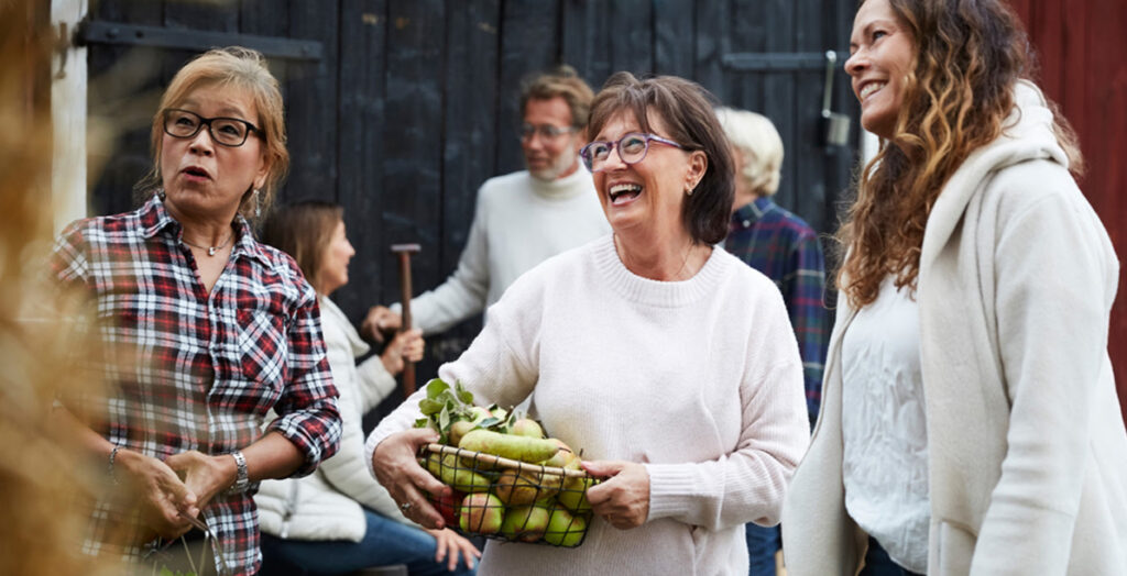 Three women stand outdoors, each holding a basket filled with fresh vegetables, showcasing their harvest.