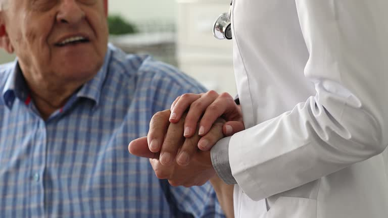 Doctor in a white coat holding hands with an elderly man in a plaid shirt.